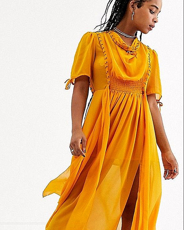 Woman wearing a yellow dress with a white background, brand 'Stilago' visible.