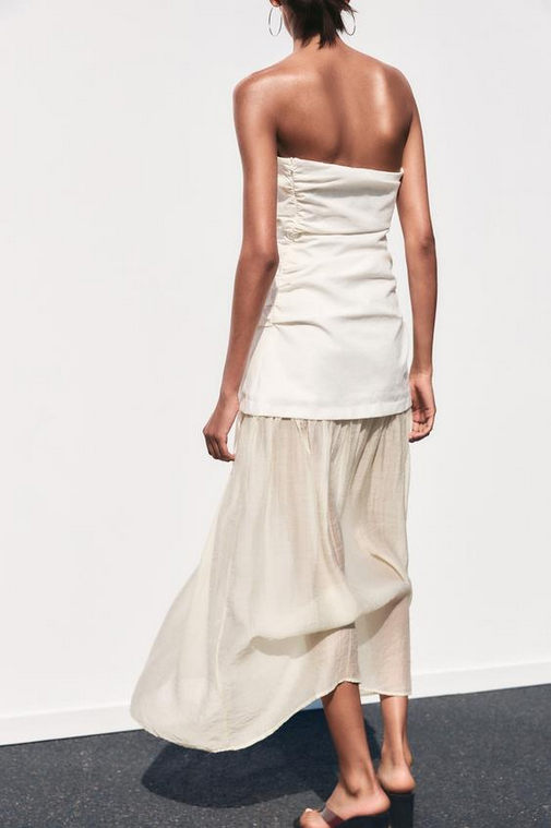 Woman wearing a strapless top and long beige skirt against a white background