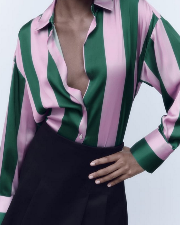 Person wearing a green and pink striped shirt with a plain background