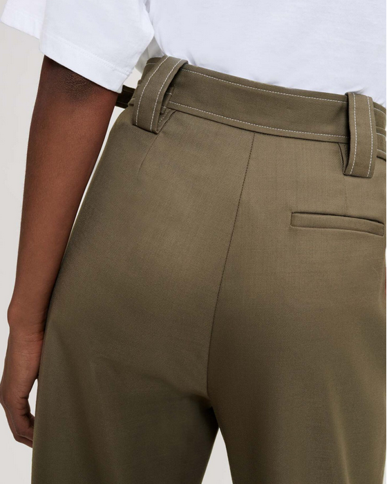 Person wearing olive green pants with a white shirt on a light background