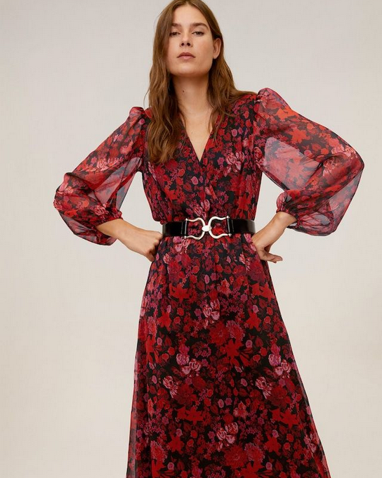 Woman wearing a red floral dress with sheer sleeves on a beige background