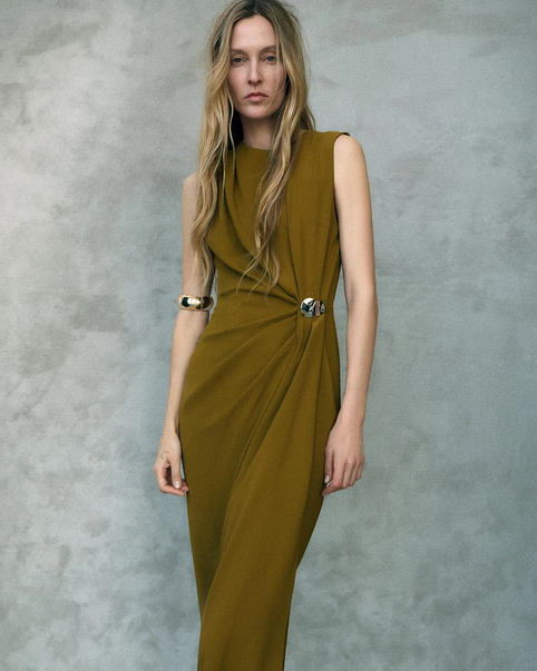 Woman wearing a sleeveless green dress against a gray background