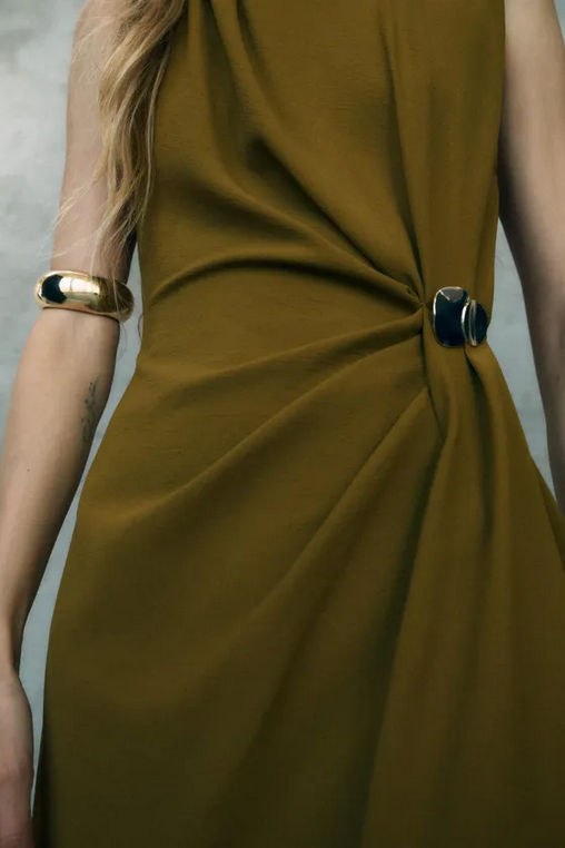 Close-up of a person wearing a mustard yellow dress with a knot detail on a plain background