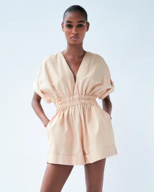 Woman wearing a beige romper against a light gray background